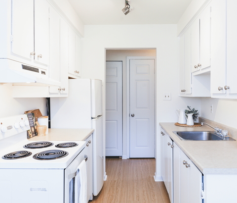 A white kitchen with a stove, sink, and cabinets.