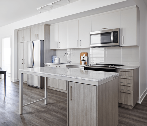 A modern kitchen with a stainless steel refrigerator, microwave, and a marble countertop.