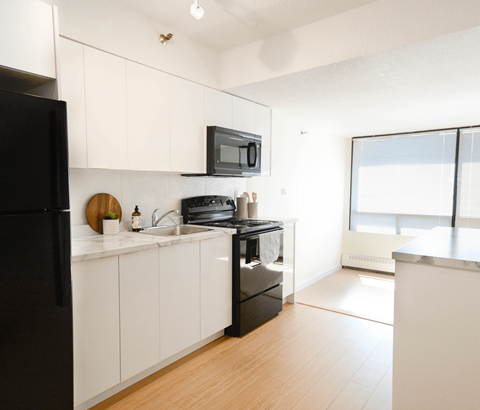 A black refrigerator is on the left in a white kitchen.