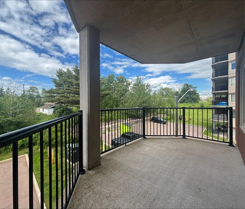 A balcony with a black railing overlooks a green lawn and trees.