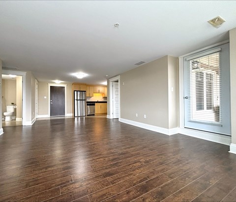 A spacious room with wooden floors and a large window with blinds.