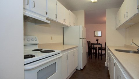 A kitchen with white appliances and brown floors.