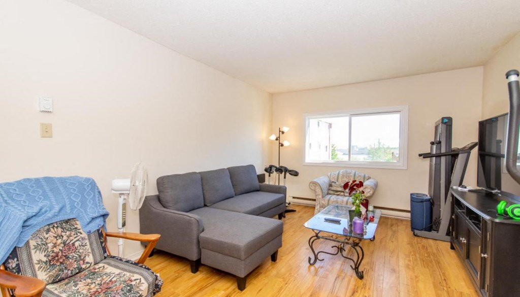 A living room with a grey couch, a chair with a floral pattern, a coffee table, and a television.