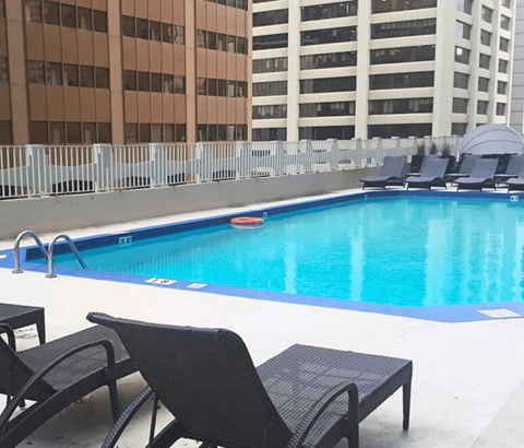 A pool with chairs around it and buildings in the background.