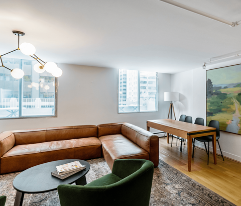 A living room with a brown leather couch, green armchair, and a painting on the wall.