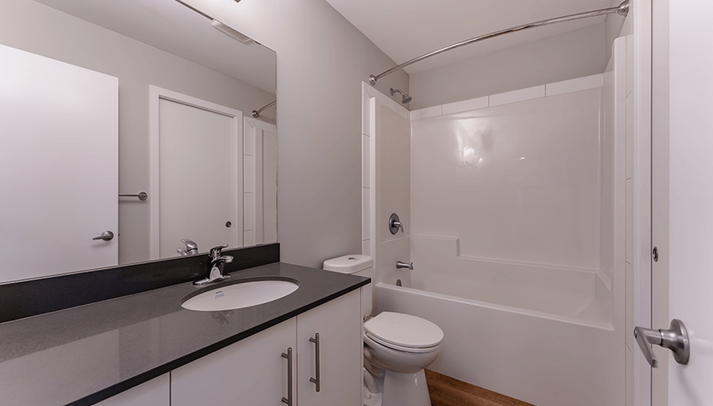 A white toilet sits in a bathroom next to a sink and a bathtub.