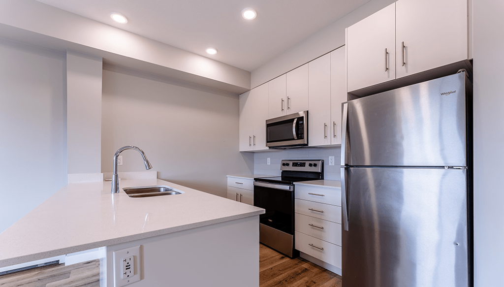 A modern kitchen with a stainless steel refrigerator, microwave, and oven.
