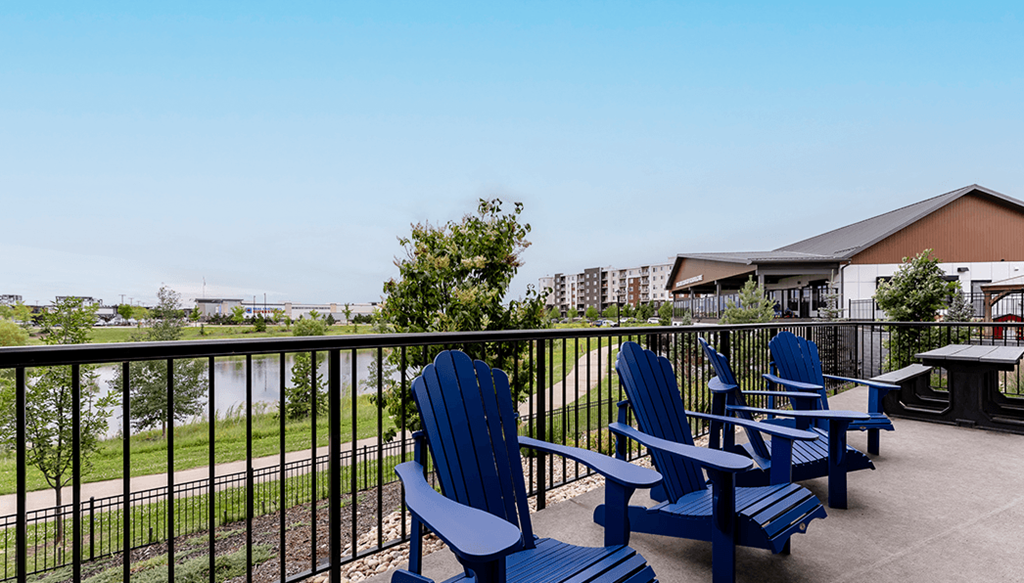 A balcony with blue chairs and a table overlooking a body of water.