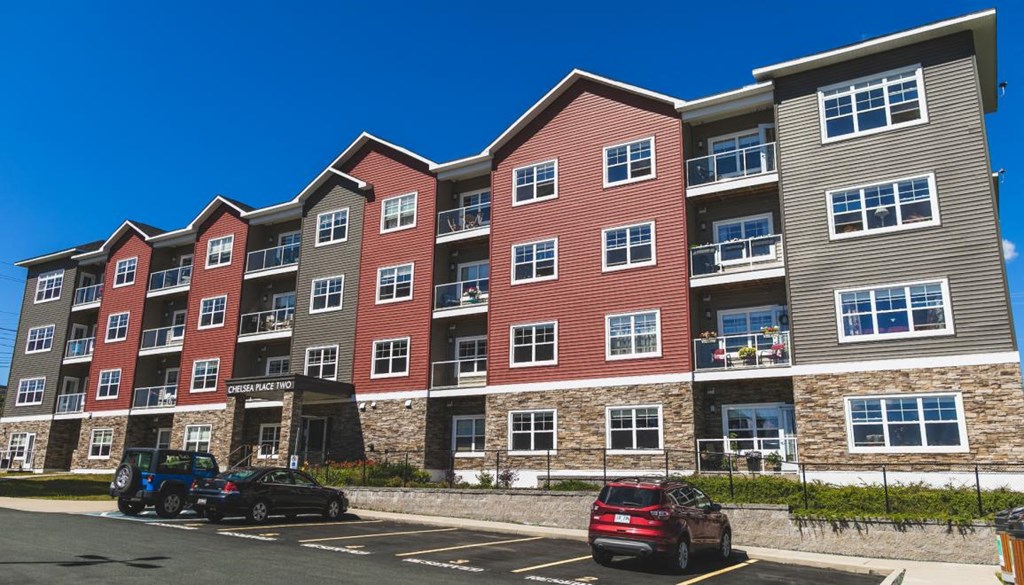 A multi-story apartment building with cars parked in front.