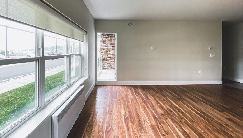 A room with wooden floors and a window overlooking a parking lot.