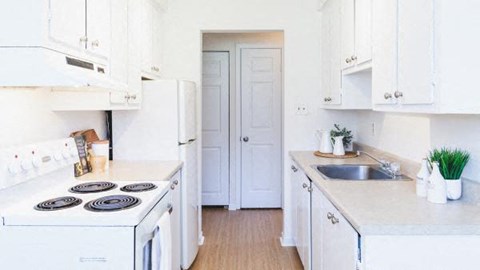 A white kitchen with a stove, sink, and cabinets.