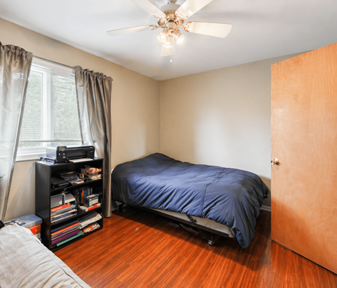 A bedroom with a bed, a ceiling fan, and a bookshelf.