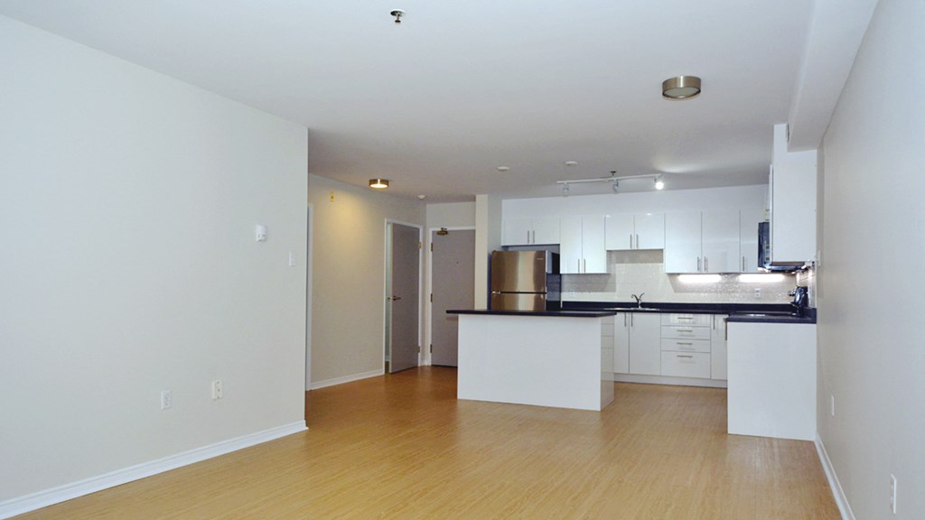 an empty living room and kitchen with white cabinets and a black counter top