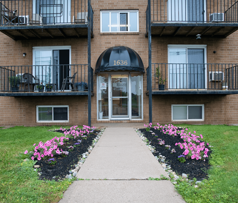 The front of apartment building number 1636 with a walkway and flower beds.