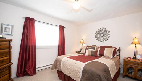 A bedroom with a bed, nightstand, and window with red curtains.