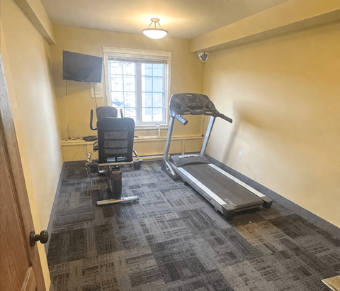 A room with a treadmill, a chair, and a television.