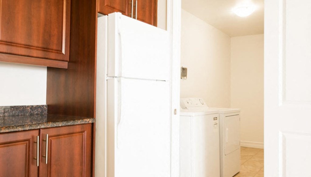 A white refrigerator stands in a kitchen next to a wooden cabinet.