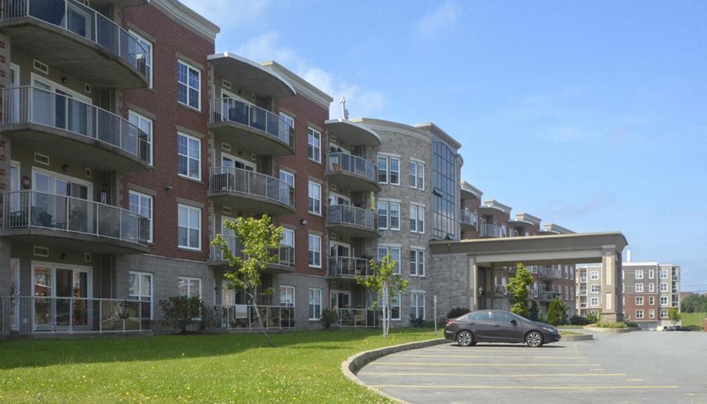 A car is parked in a parking lot in front of apartment buildings.