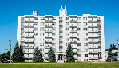 A large white apartment building with balconies and a green lawn in front.