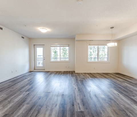 A spacious room with wooden floors and two windows.