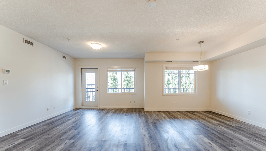 A large empty room with wooden floors and two windows.