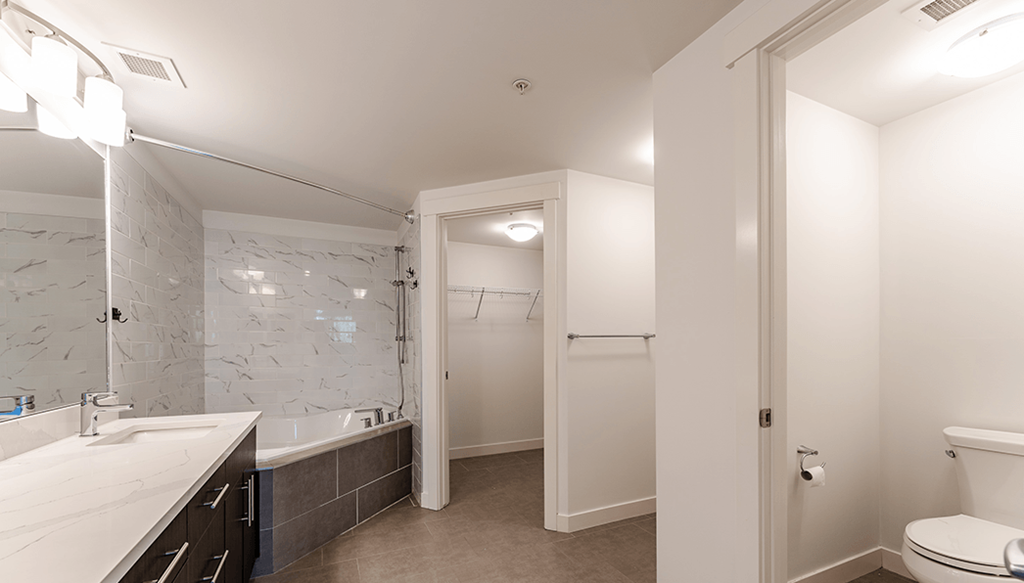 A white bathroom with a marble counter top and a walk in shower.