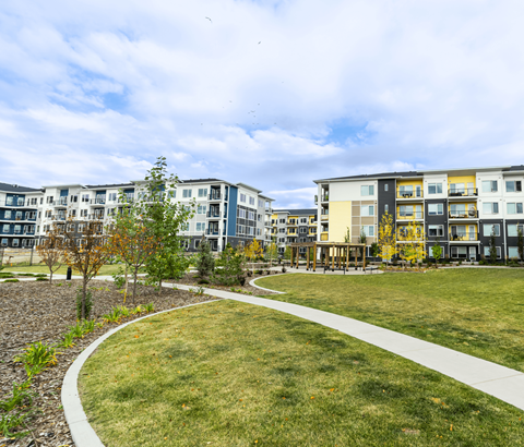 A grassy area with a walkway and apartment buildings in the background.