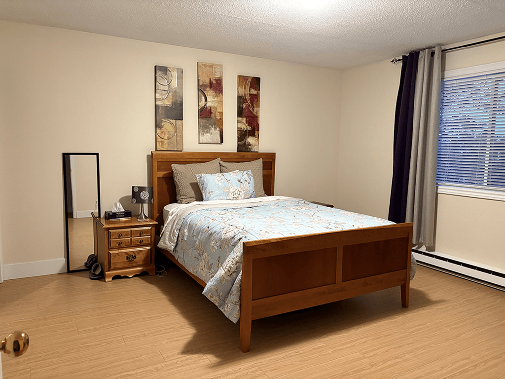 A bedroom with a bed, nightstand, and a painting on the wall.