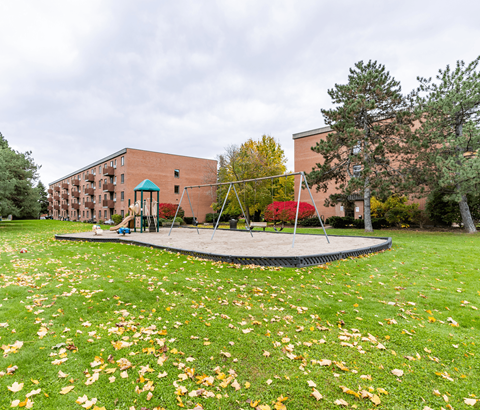A playground with a trampoline and a slide in front of a brick building.