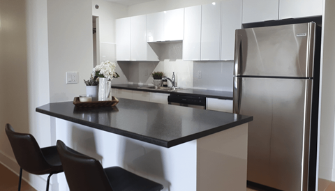 A kitchen with a black countertop and a stainless steel refrigerator.