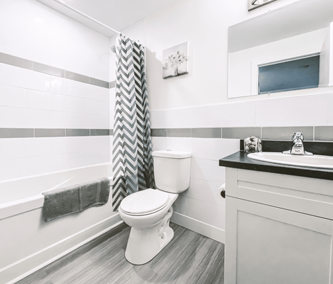 A white toilet in a bathroom with a grey and white shower curtain.