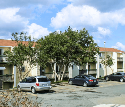 A silver minivan is parked in a parking lot in front of a white apartment building.