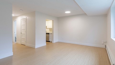 an empty living room and kitchen with white walls and wood flooring