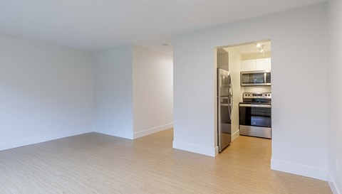 an empty living room with a kitchen in the background