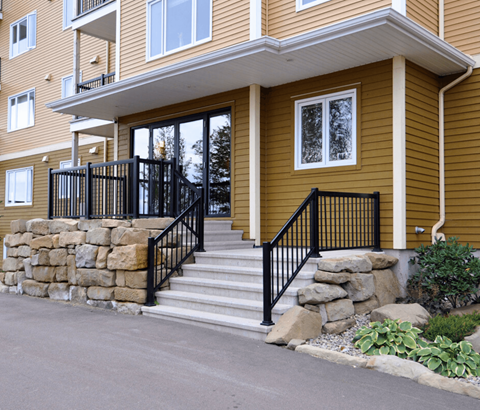 A brown house with a black railing on the stairs.