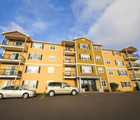 Two cars parked in front of a yellow apartment building.