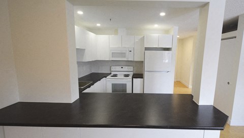 an empty kitchen with a black counter top and white appliances