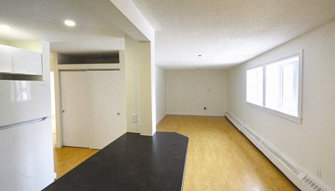 an empty living room with a refrigerator and a window