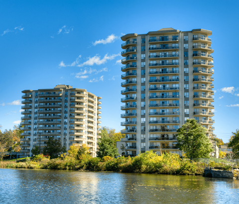 Two tall residential buildings are situated next to a body of water.
