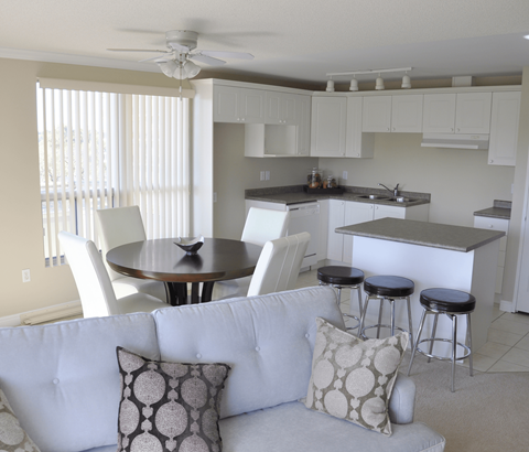 A white couch with a round table and bar stools in a kitchen.