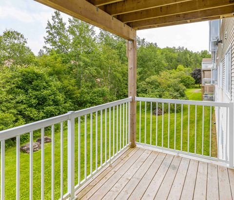 A wooden deck with a white railing overlooks a lush green yard.