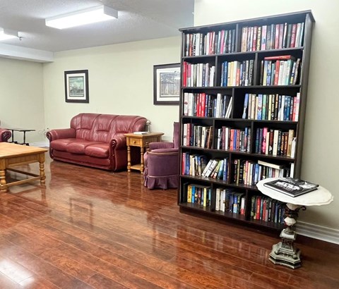 A room with a red couch, a wooden table, a chair, a bookshelf, and a round table with a book on it.
