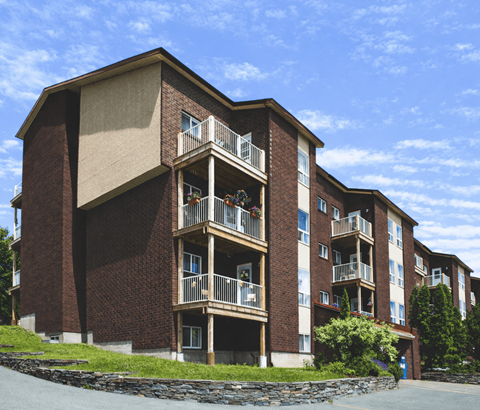 A large brick building with balconies and a stone wall in front.