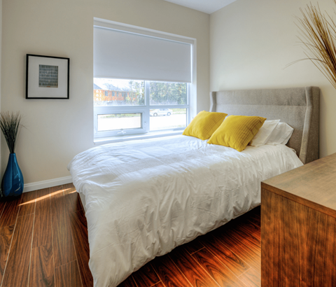 A bedroom with a bed, wooden nightstand, and a window with blinds.
