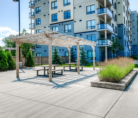 A patio area with a table and benches under a pergola in front of a building.