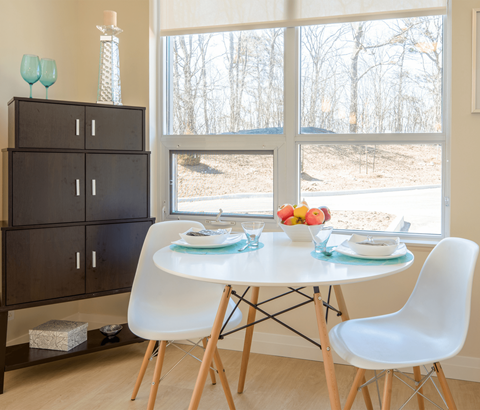 A dining room with a white table and chairs, a cabinet, and a view of trees outside the window.