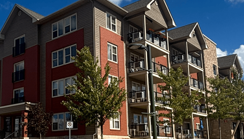 A red and grey apartment building with balconies and trees in front.