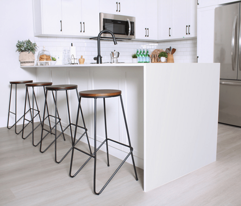 A kitchen with white cabinets and a white island with bar stools.