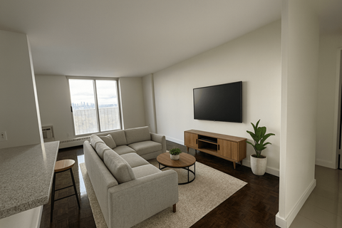 A living room with a grey couch and a flat screen TV mounted on the wall.