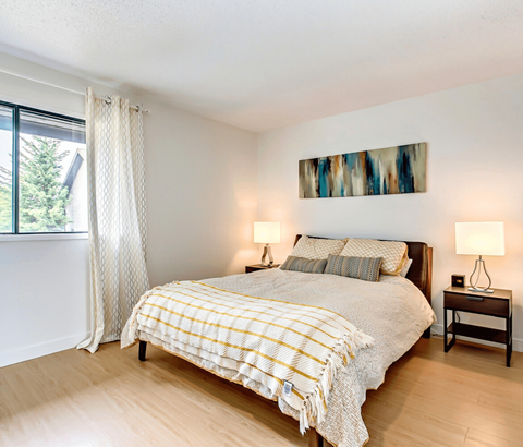 A bedroom with a bed, two lamps, and a painting on the wall.